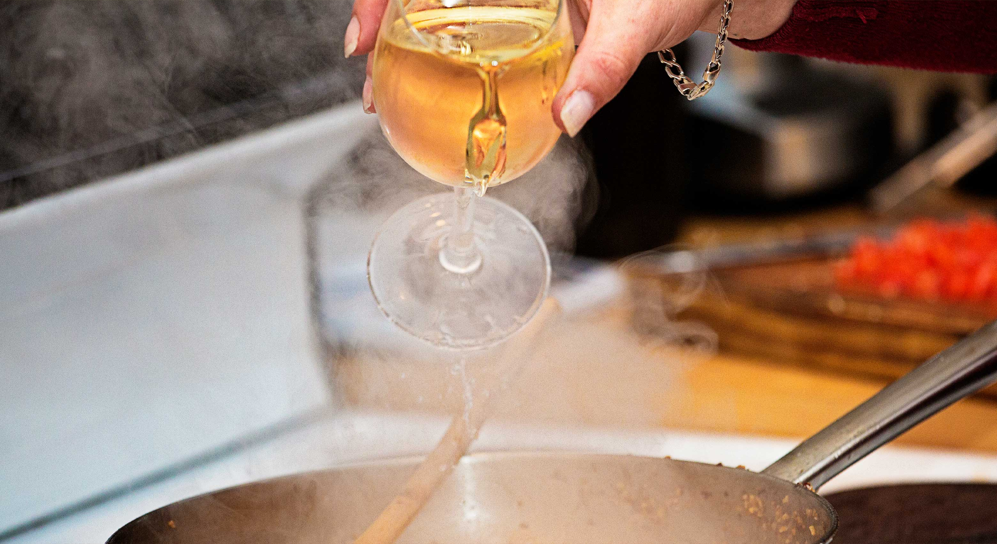 Wine being poured into a cooking pot over a stove.