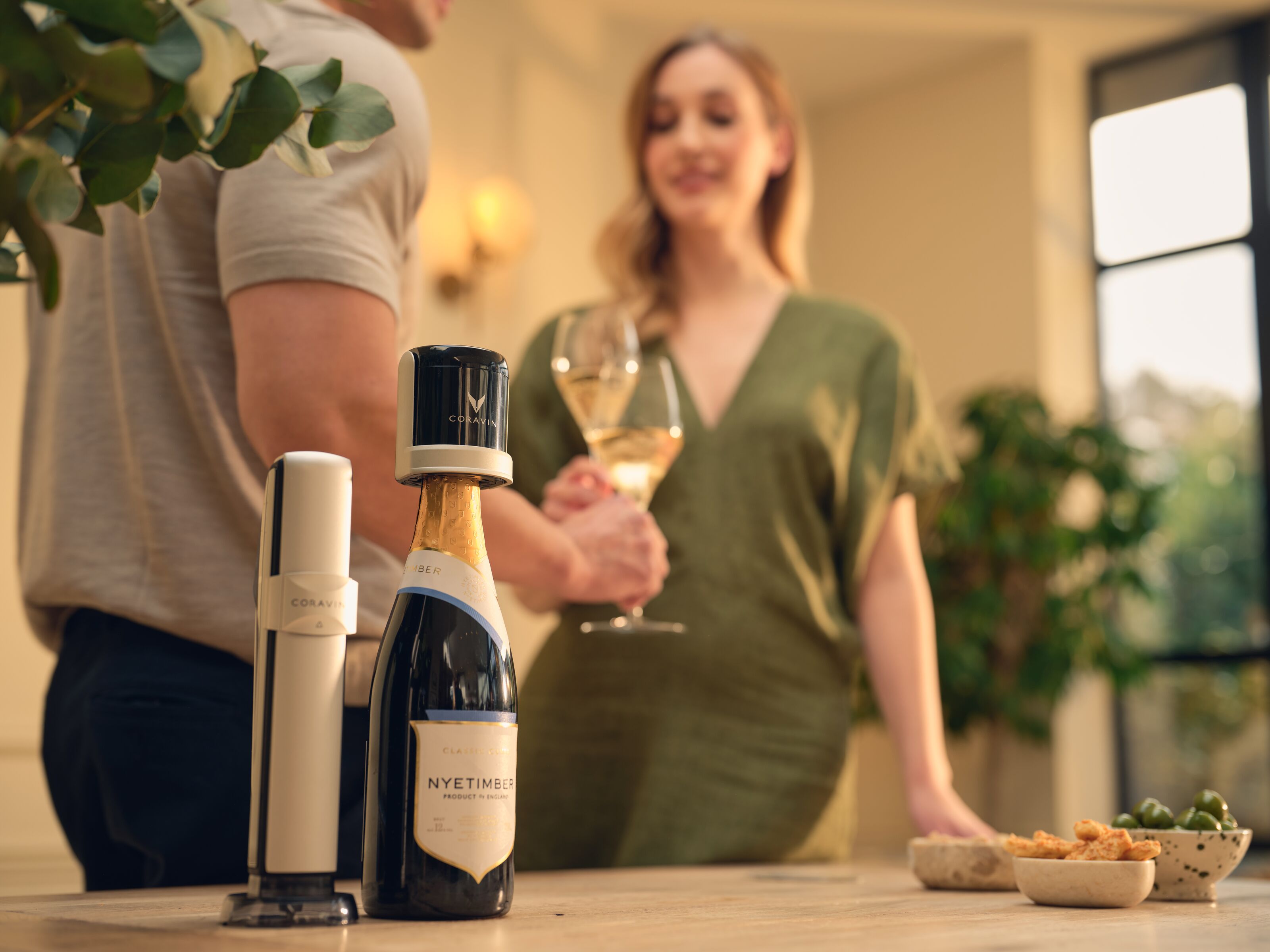Two people standing behind a table with wine bottles and glasses, blurred background